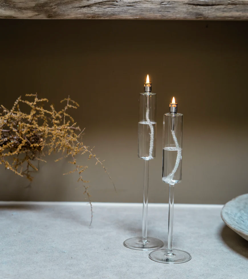 Two clear glass candle holders with lit candles on a neutral background