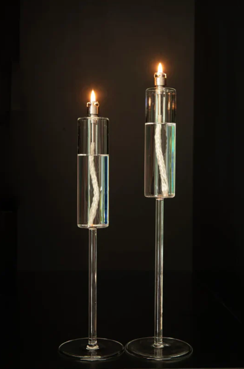 Two tall, clear glass candle holders with lit candles against a dark background