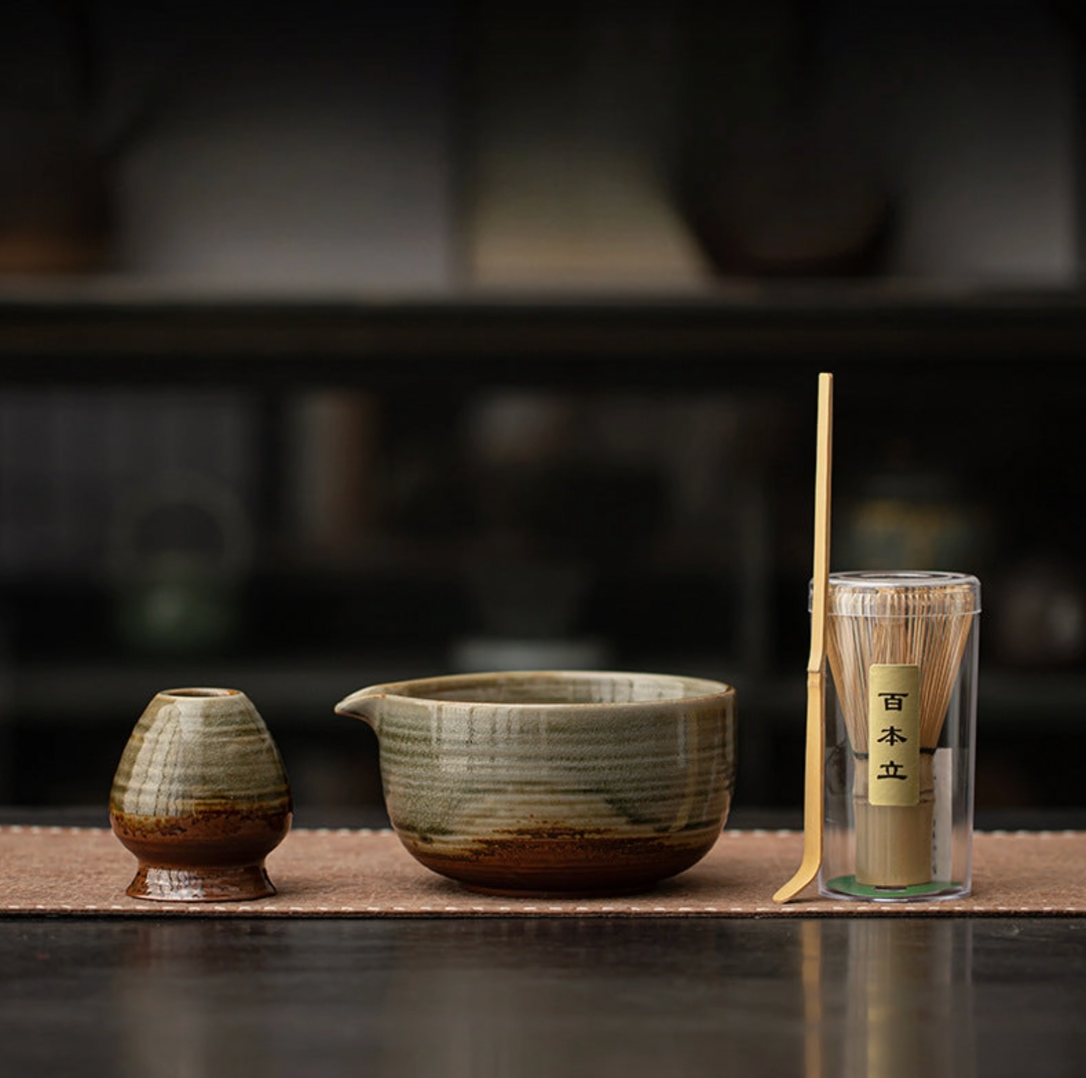 Tea-making set with ceramic teapot, small container, and scoop on a dark surface.