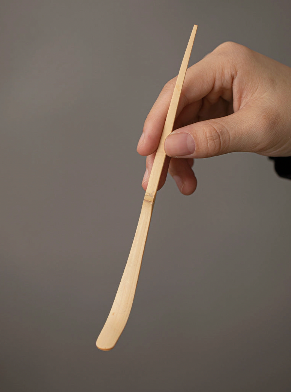 Hand holding a wooden spoon against a gray background