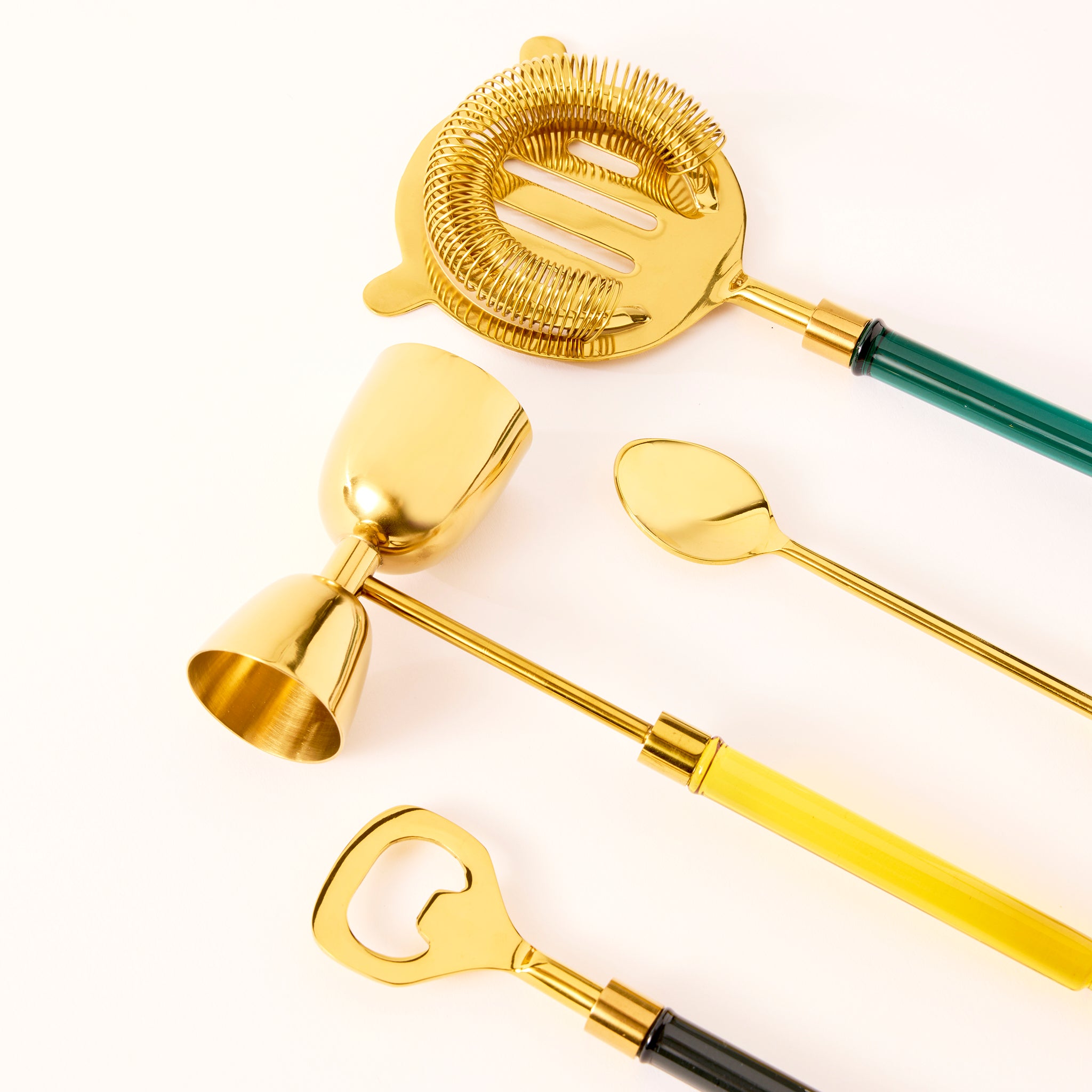 Set of gold cocktail tools including a strainer, jigger, and bottle opener on a white background