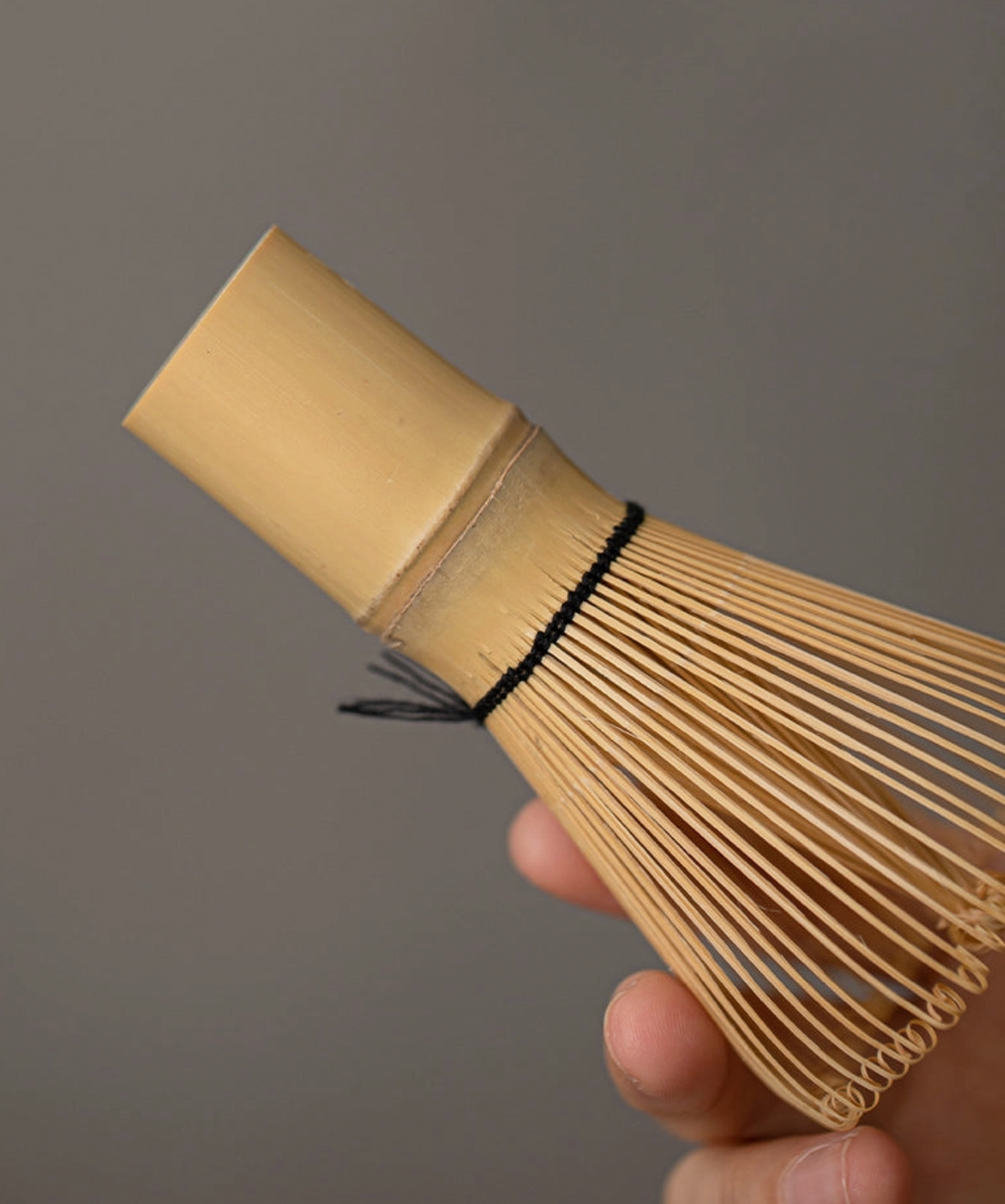 Bamboo whisk held by a hand against a gray background