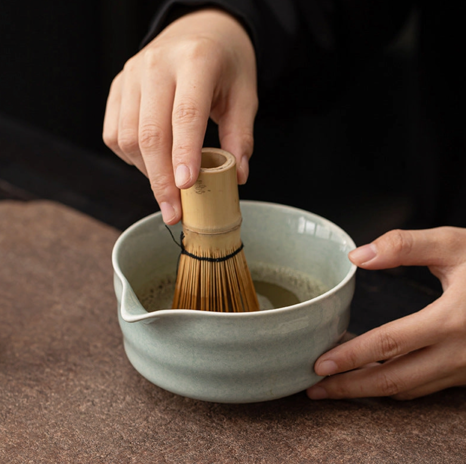 Person using a bamboo whisk to prepare matcha in a ceramic bowl.