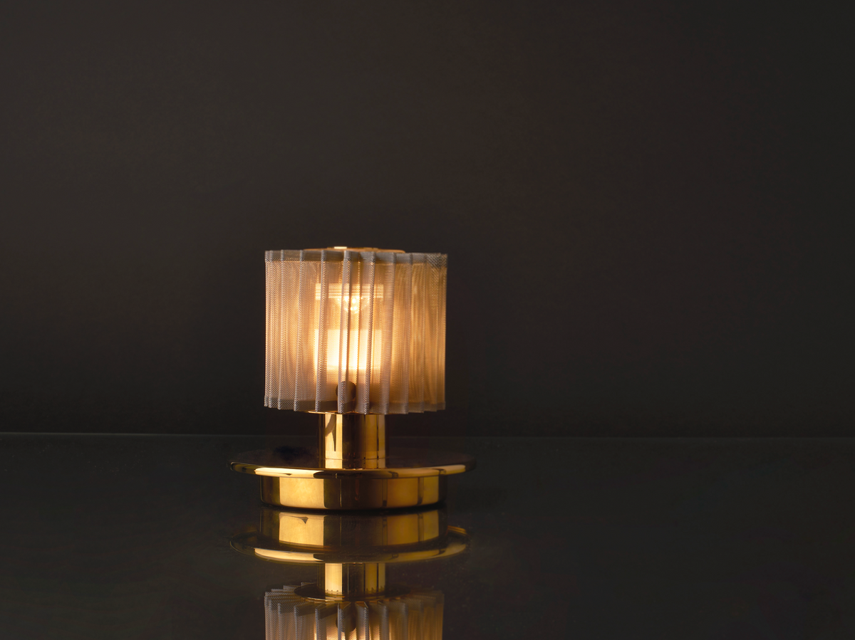 Small table lamp with a textured shade on a reflective surface against a dark background