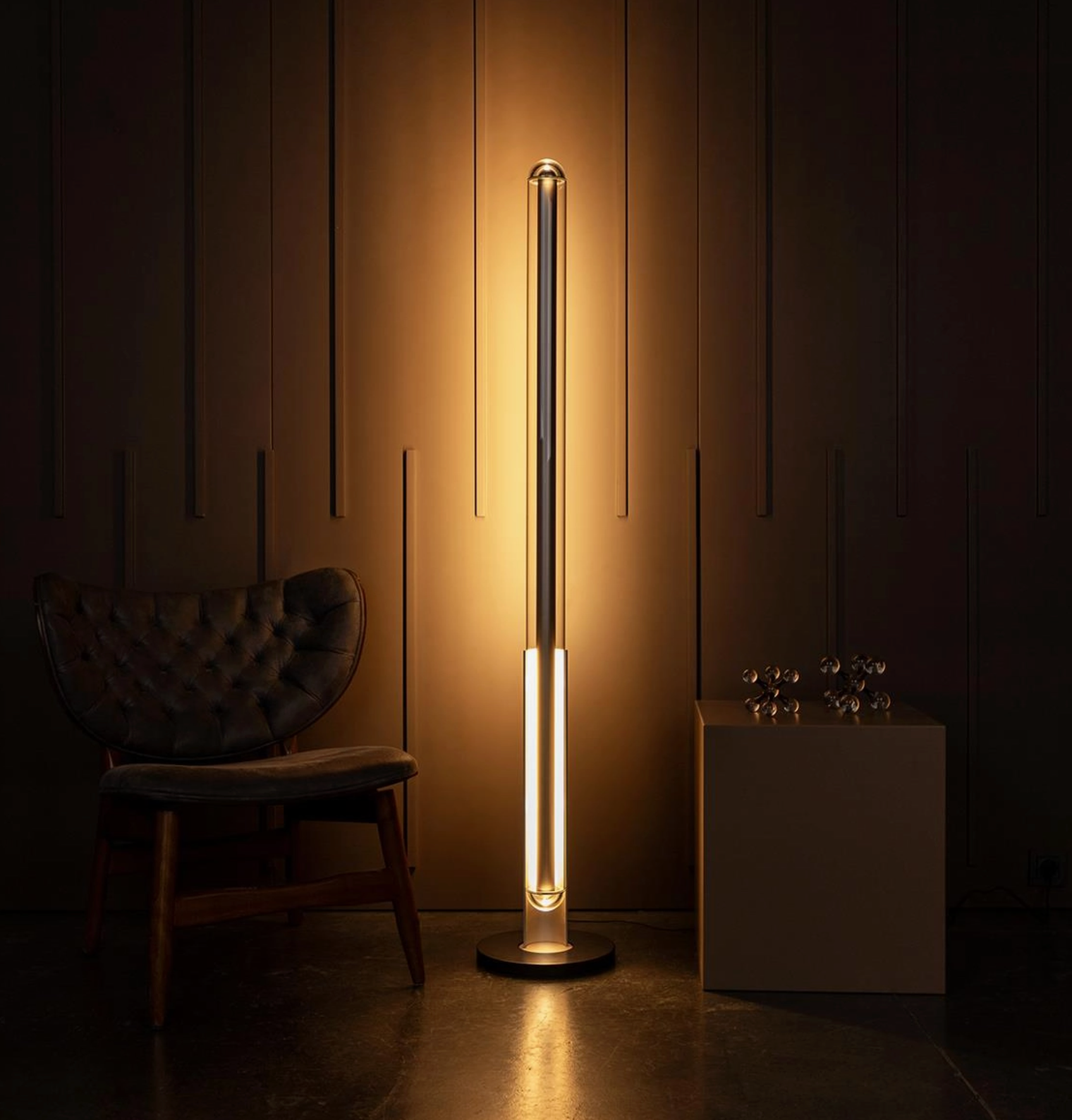 Modern floor lamp casting a warm glow in a dimly lit room with a chair and decorative items.