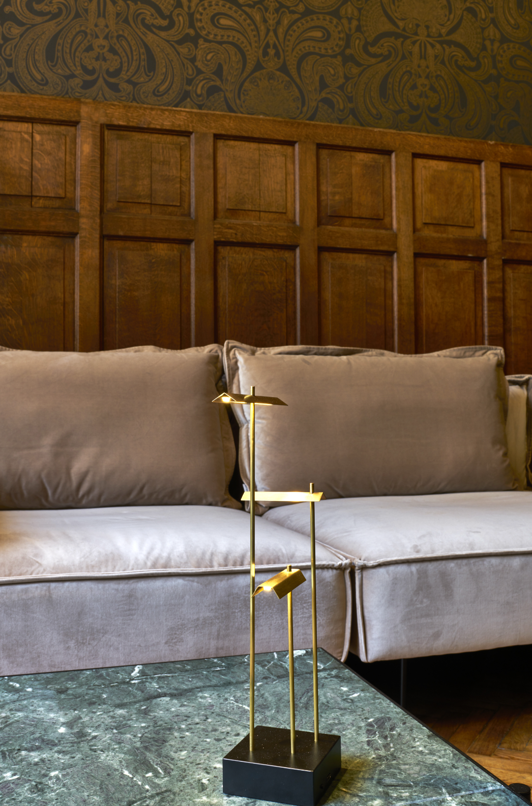 Gold decorative stand on a marble coffee table with a gray sofa and wooden wall in the background