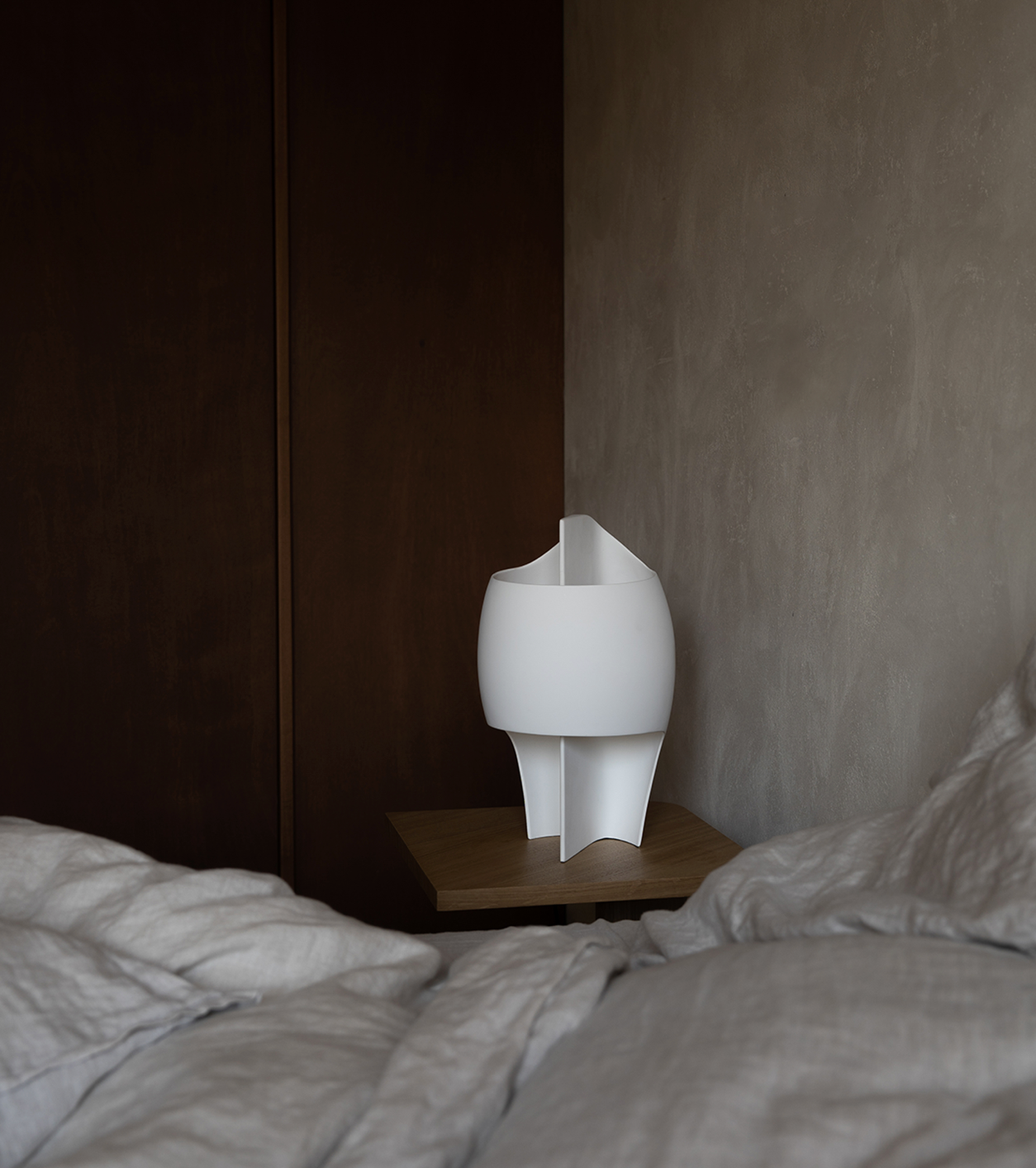 White lamp on a bedside table next to a bed with gray bedding.