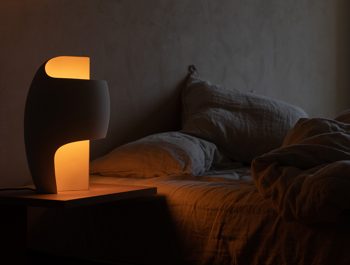Modern table lamp on a bedside table with a cozy bedroom setting.