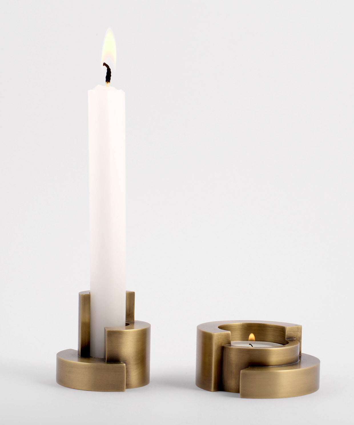 Set of two brass candle holders with candles on a light gray background