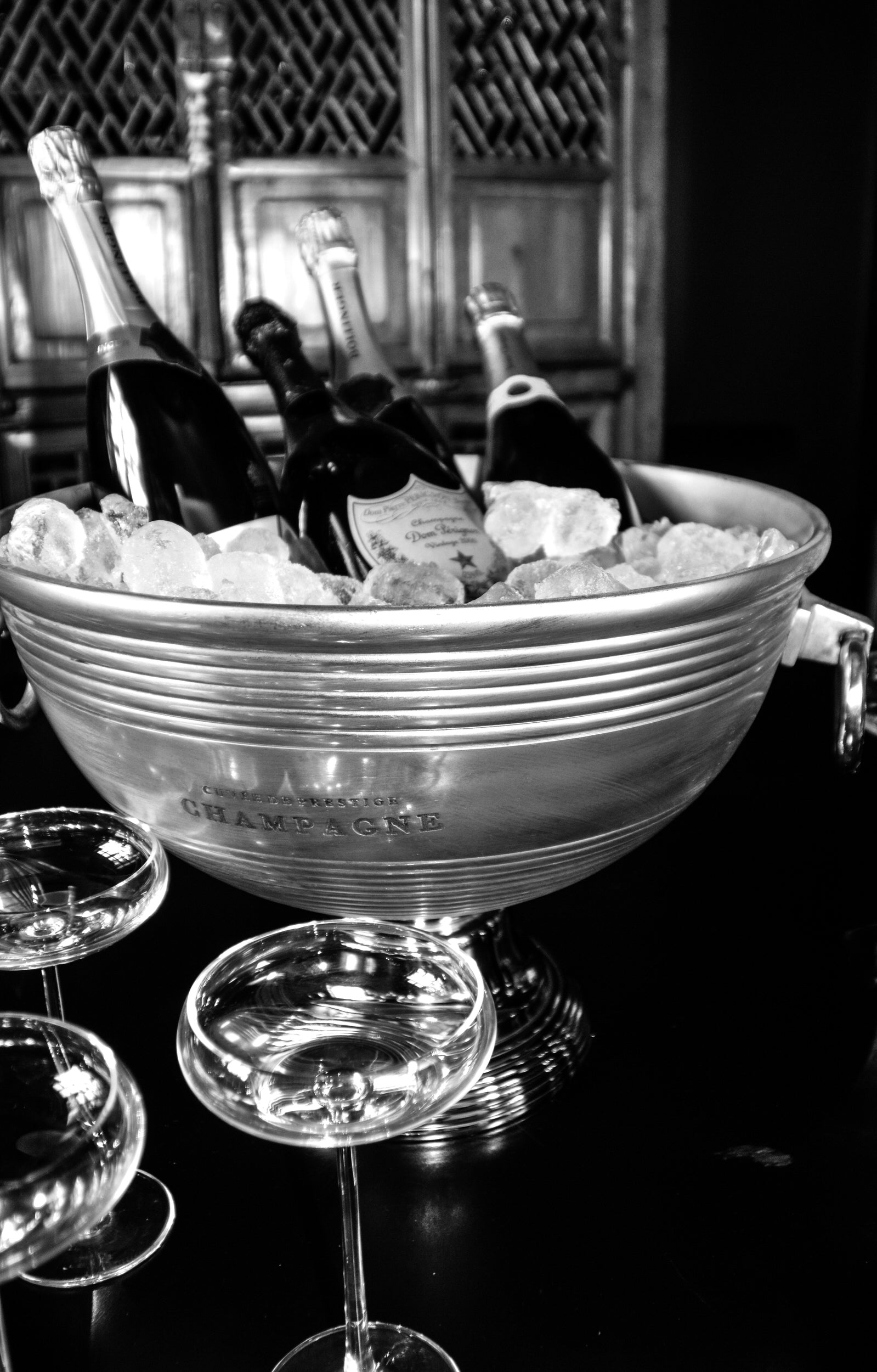 Bottles of champagne in an ice bucket with glasses around, black and white photo