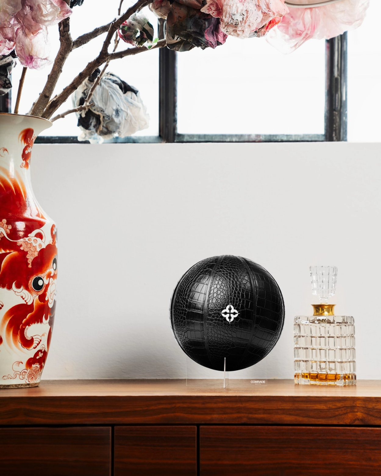 Black decorative sphere on a wooden surface with a vase and flowers in the background