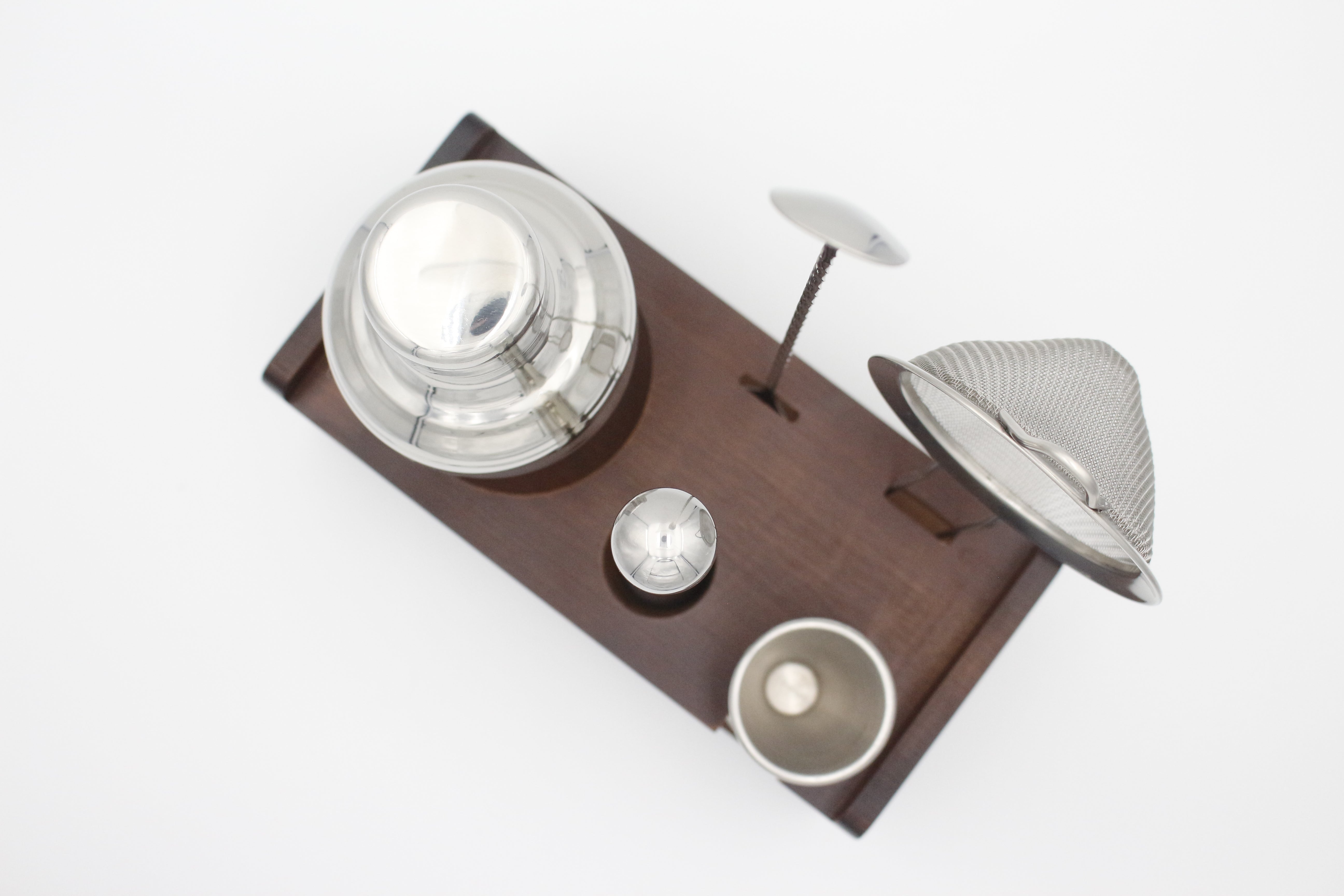 Set of metallic kitchen utensils on a wooden tray with a white background