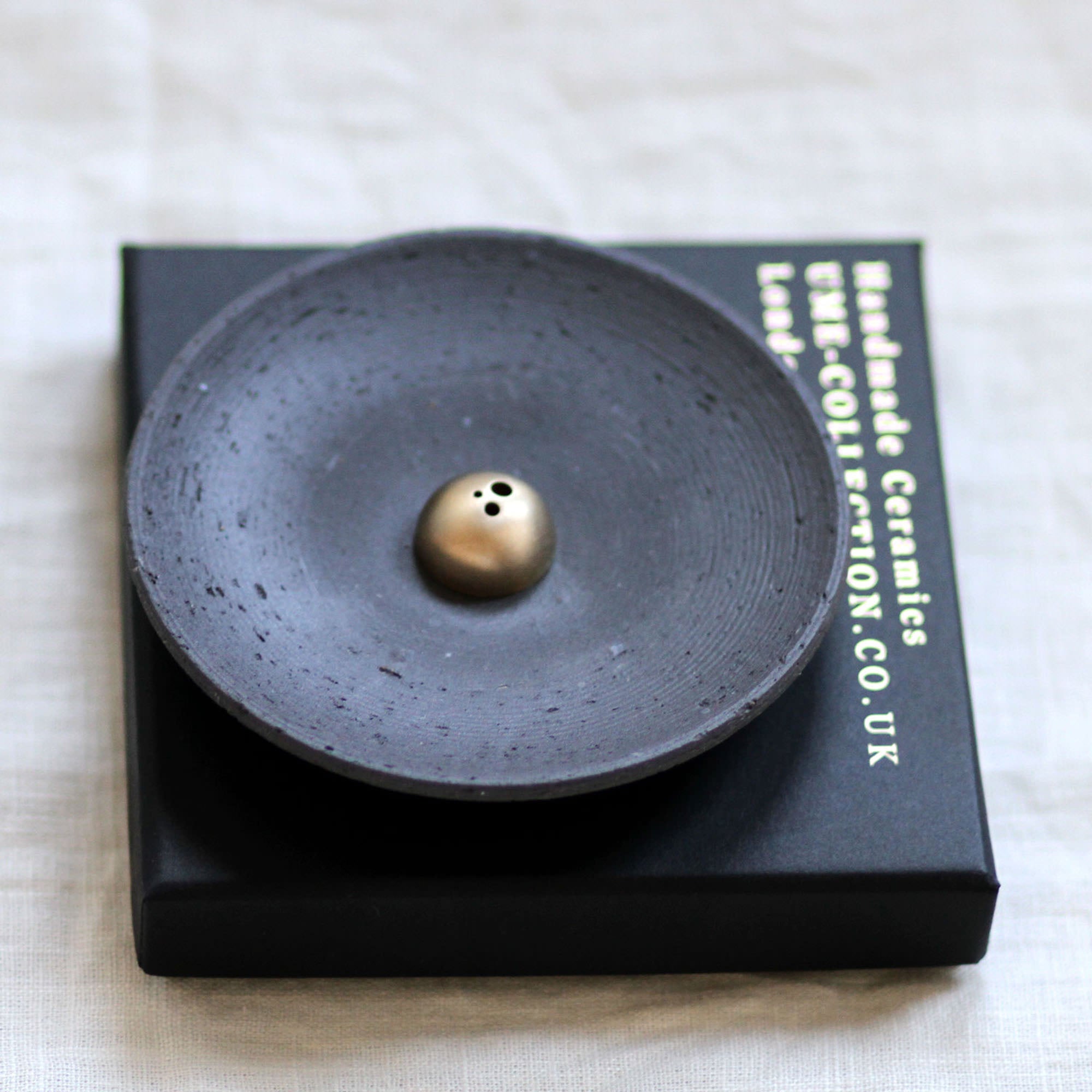 Ceramic incense burner with gold accent on a black box, brand 'Handmade Ceramics' visible