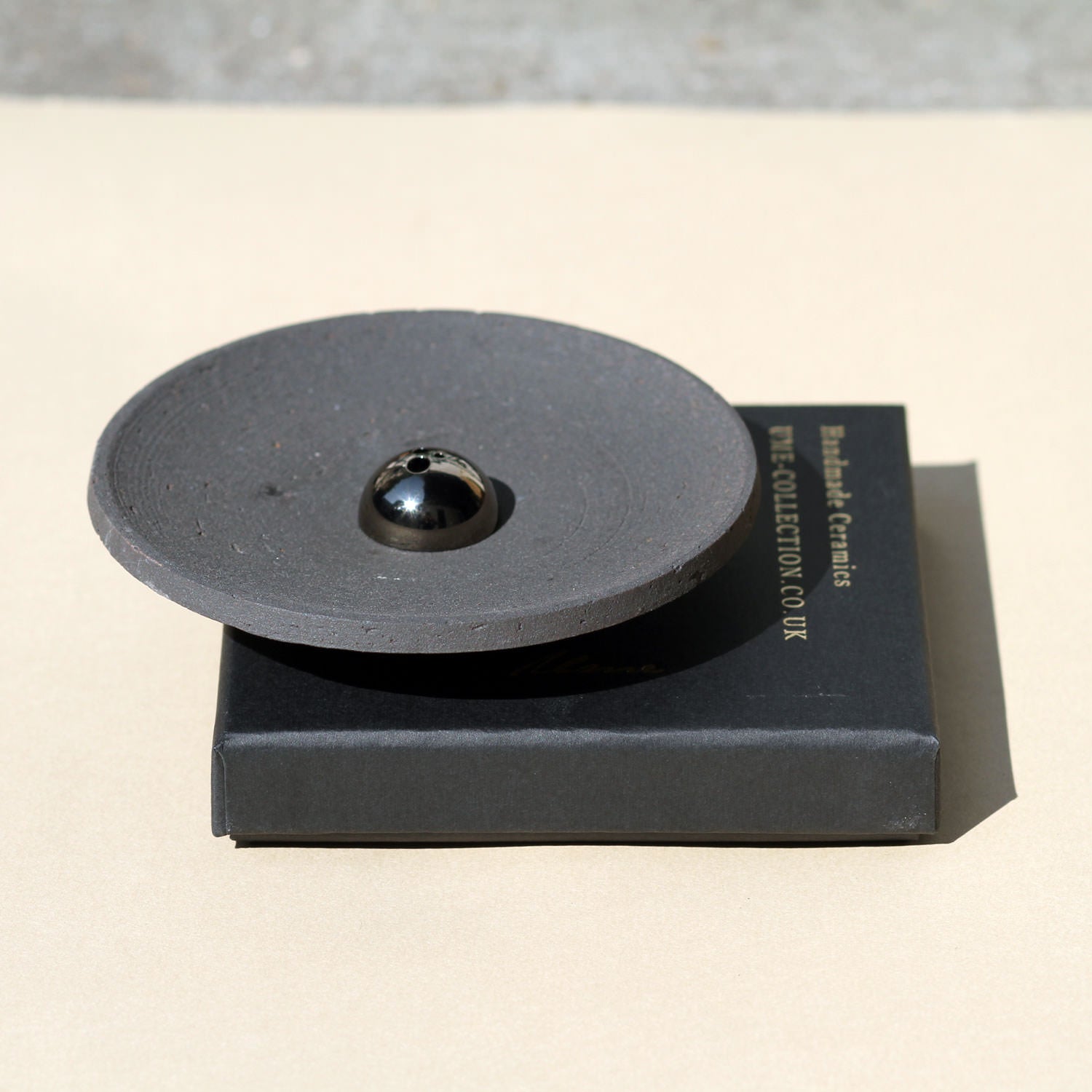 Black ceramic disc on a black stand with 'Birks & Co. Collection' text on a beige surface.