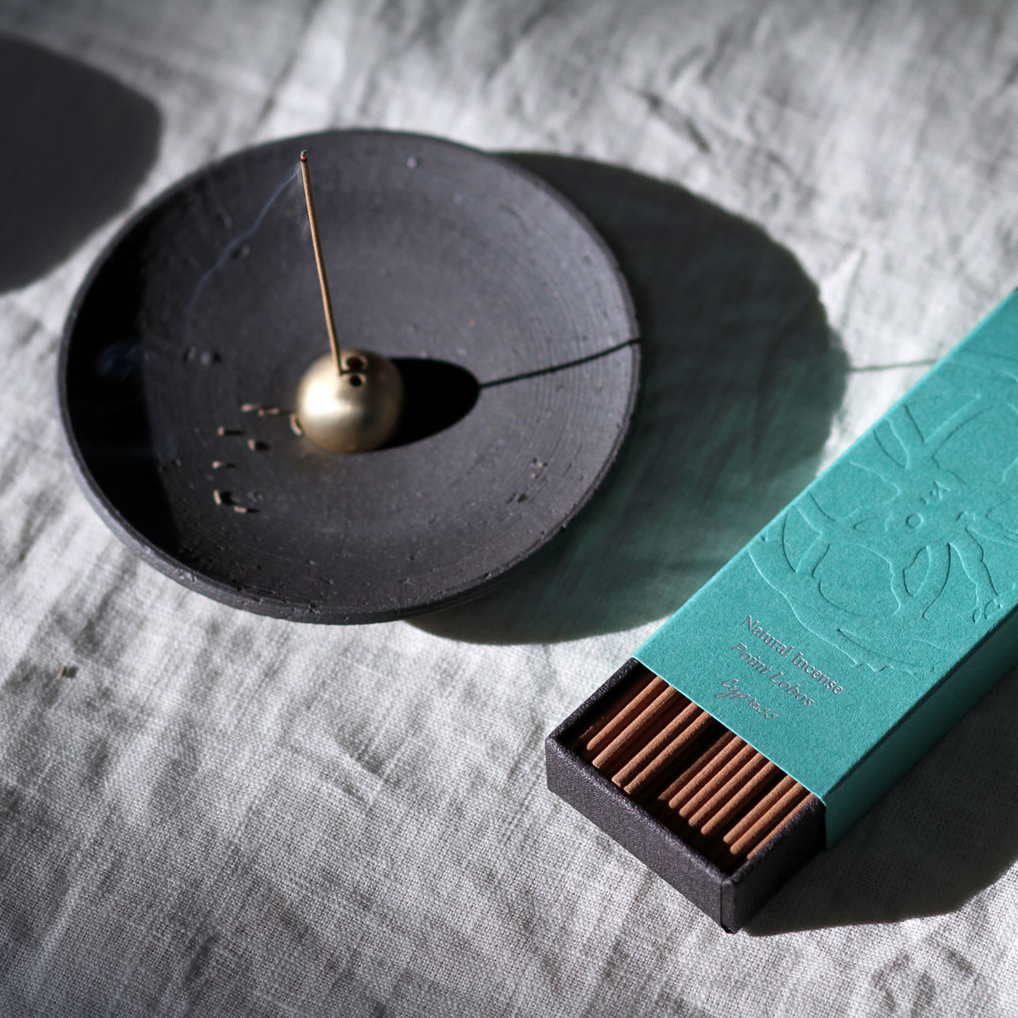 Incense holder with a gold incense stick and a teal box of incense on a textured surface.