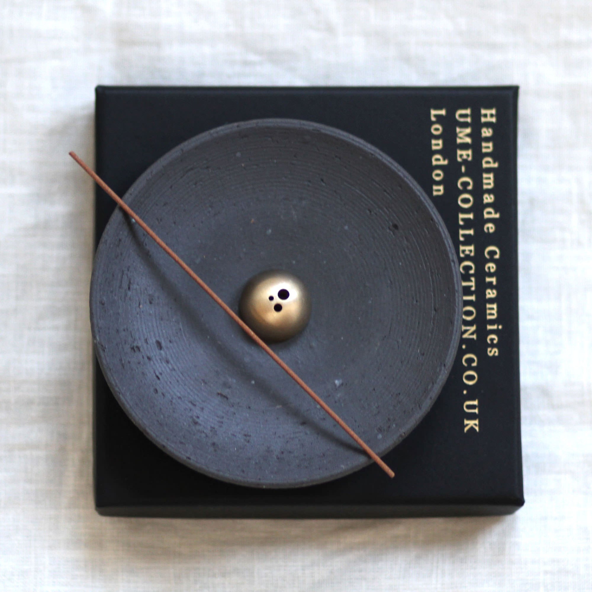 Ceramic incense burner with a gold ball and stick on a black box labeled 'UME Collection Co. UK'.