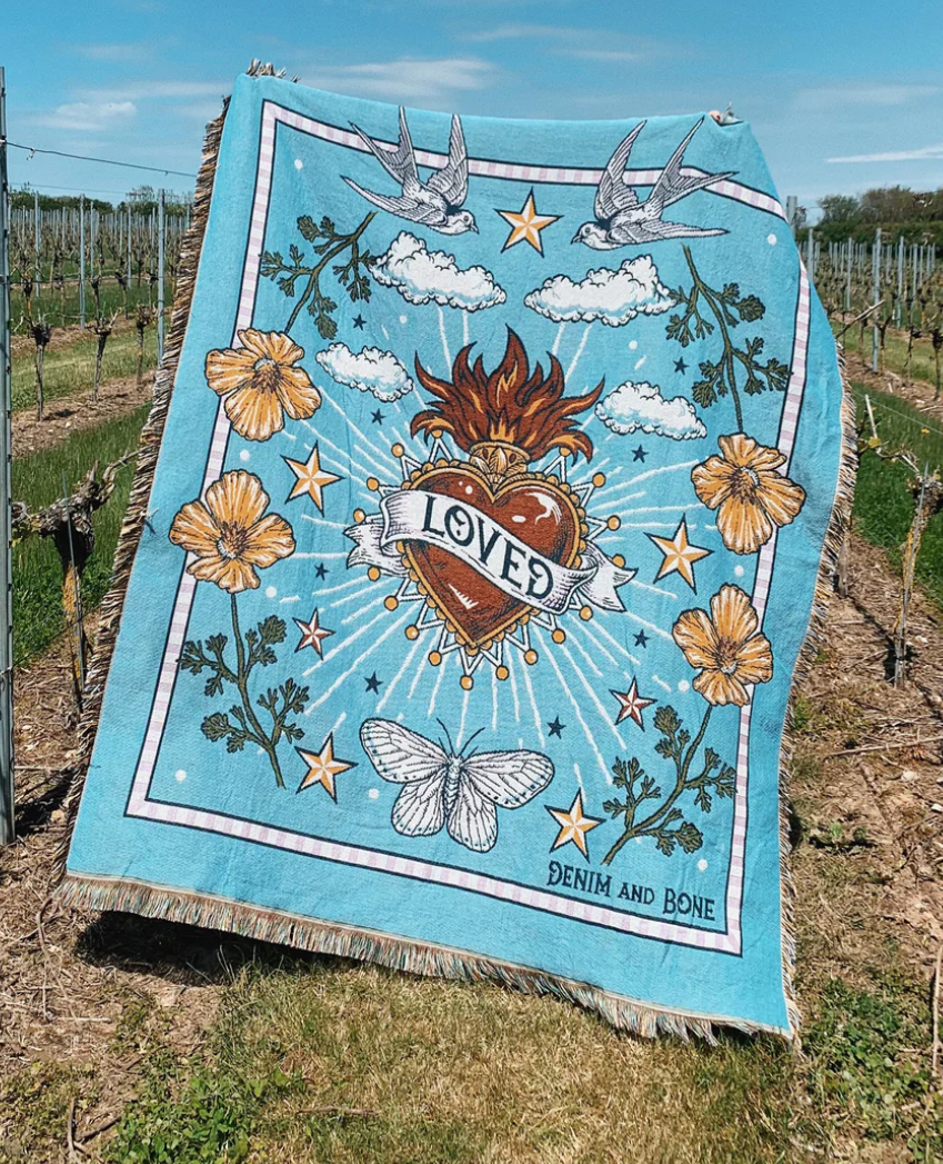 Decorative blanket with artistic design featuring a heart and flowers, set against a vineyard background.
