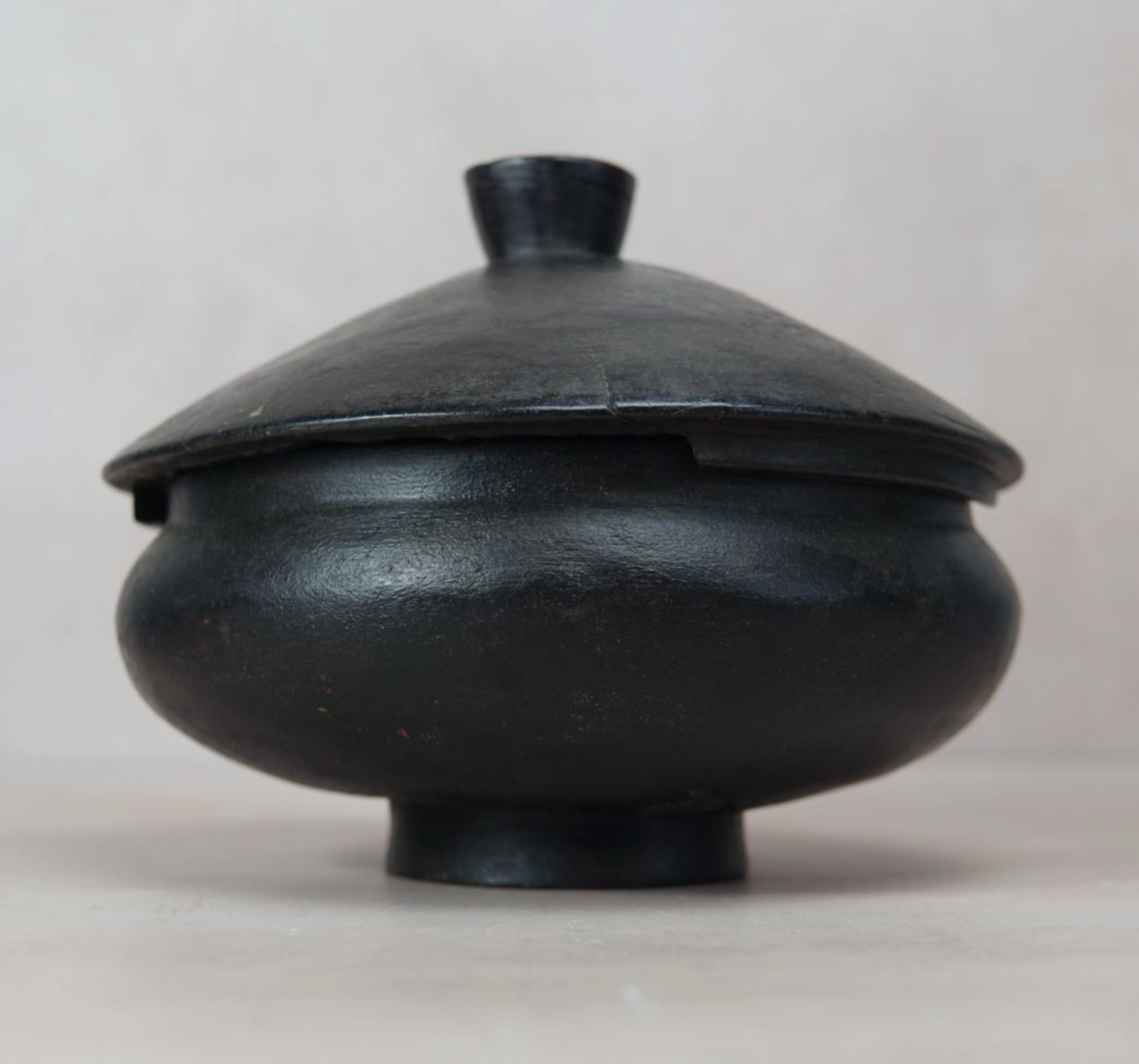 Black ceramic pot with lid on a light gray background