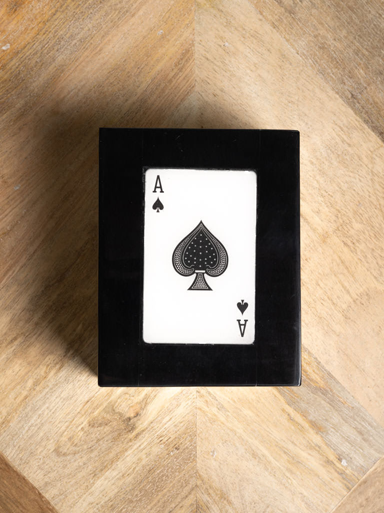 Playing card, specifically the Ace of Spades, framed in black on a wooden surface.