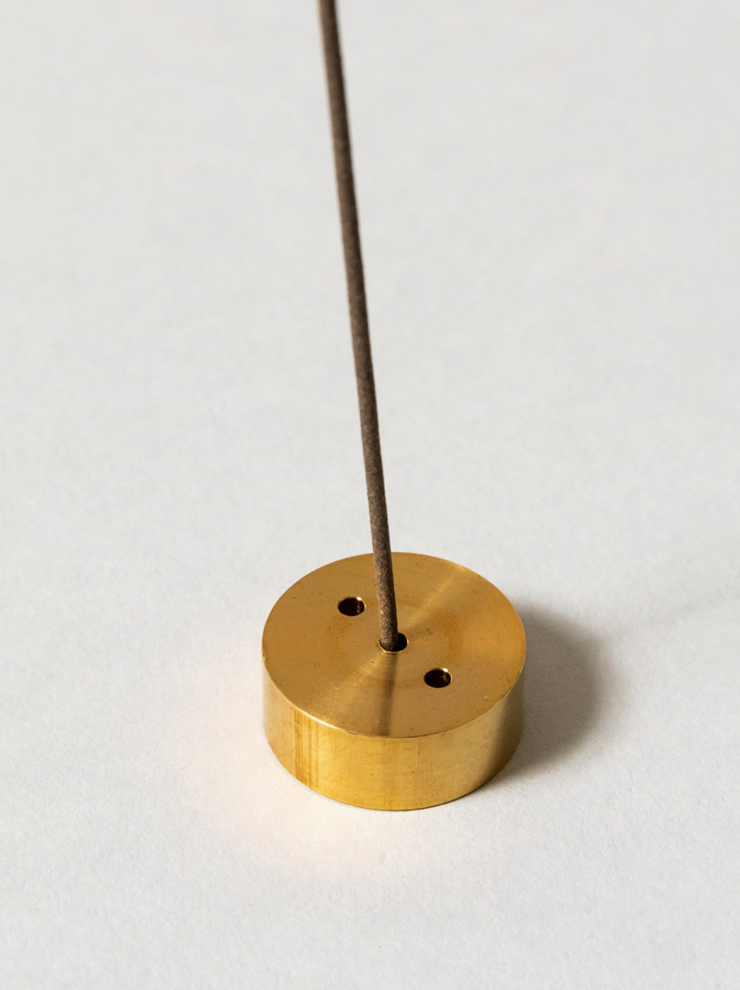Brass incense holder with a single incense stick on a white background