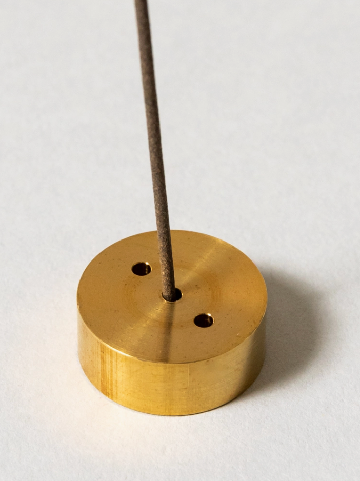 Brass incense holder with a single incense stick on a white background