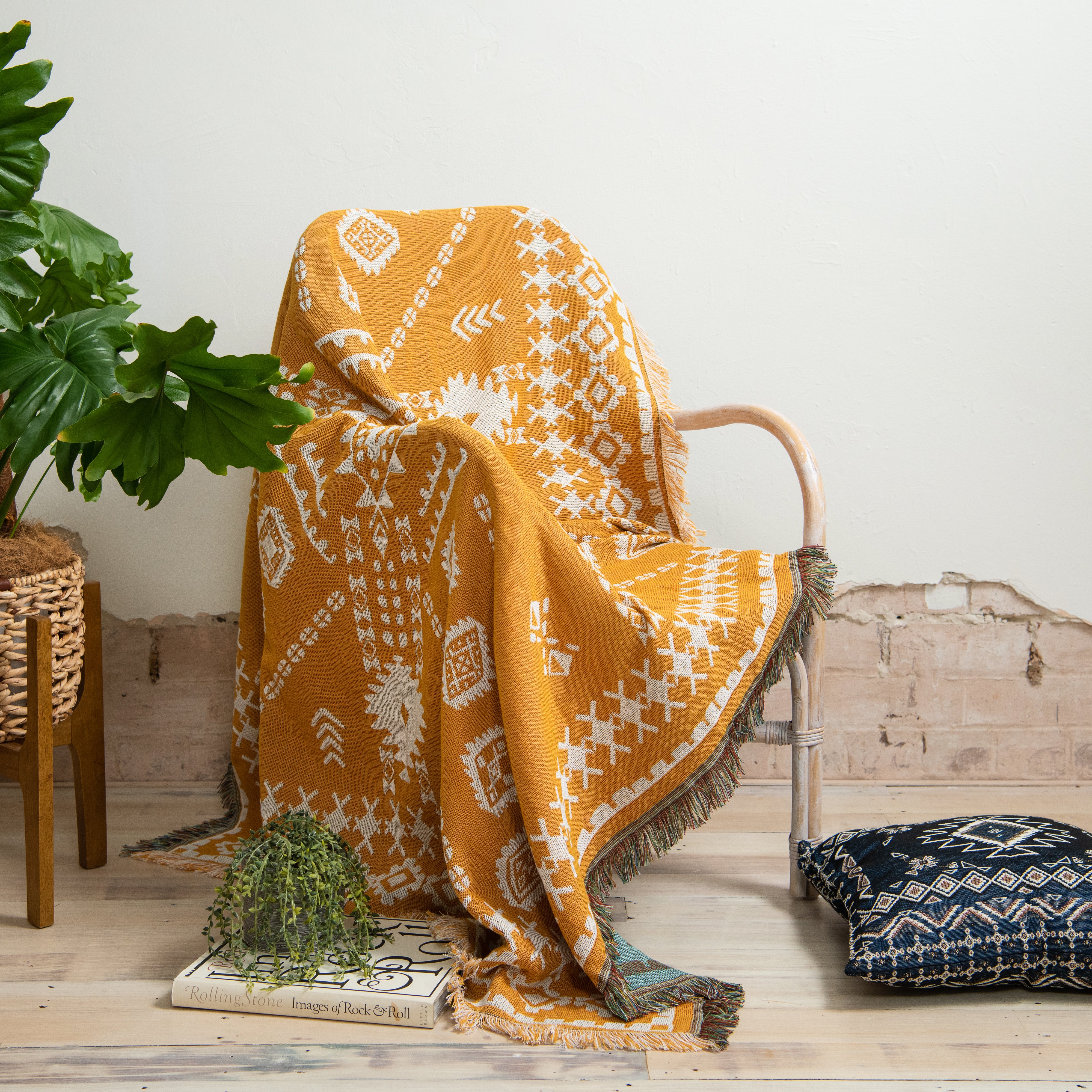Yellow patterned blanket draped over a chair with a plant and pillow in the background