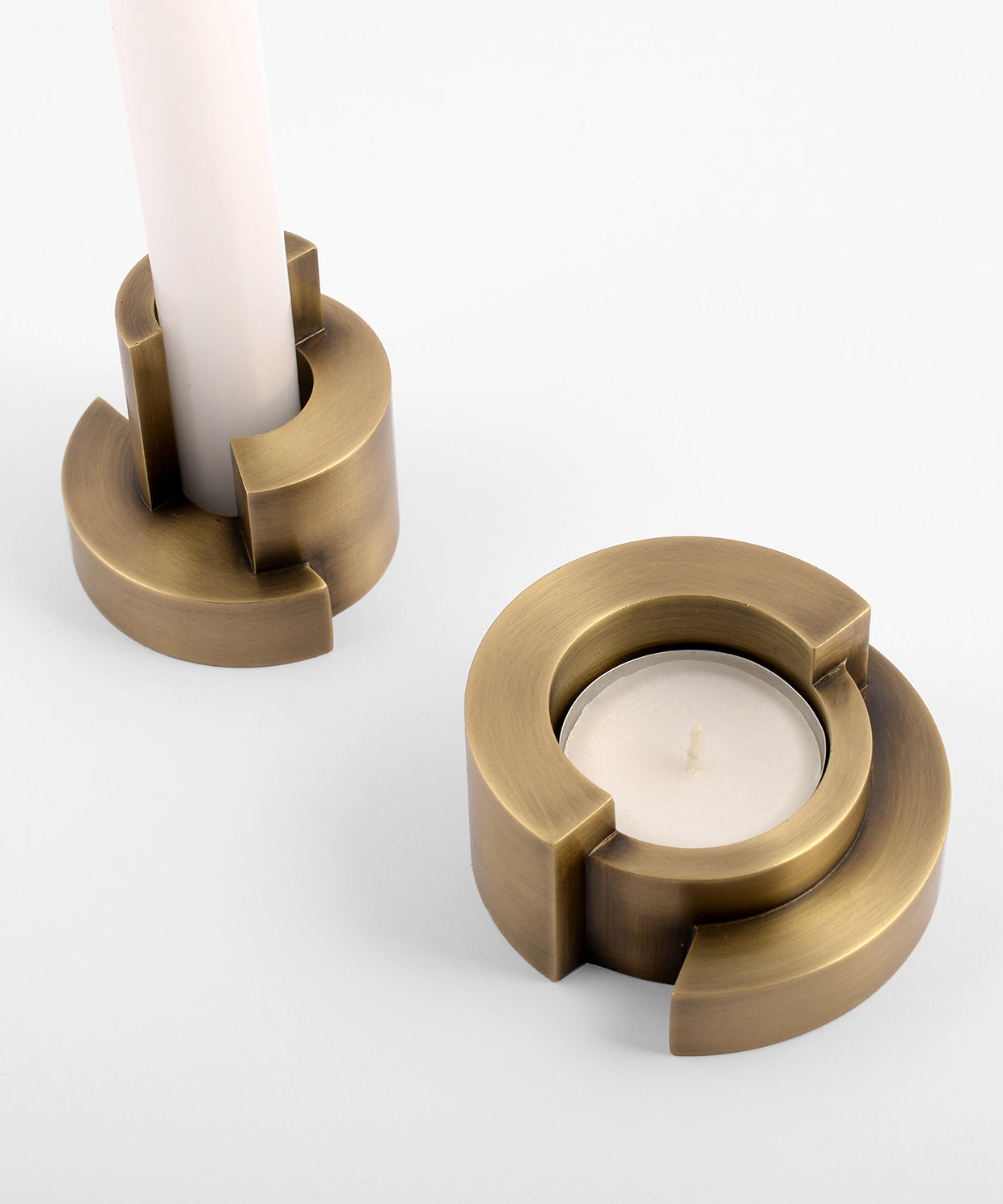 Two brass candle holders with candles on a white background