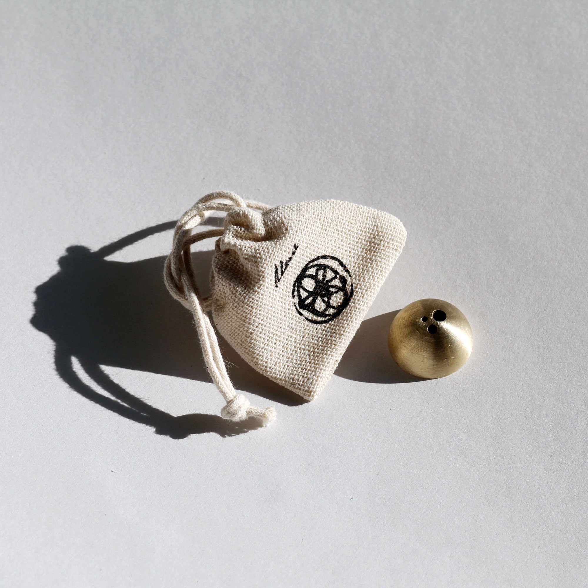 Small beige drawstring bag with a black symbol next to a brass object on a gray background