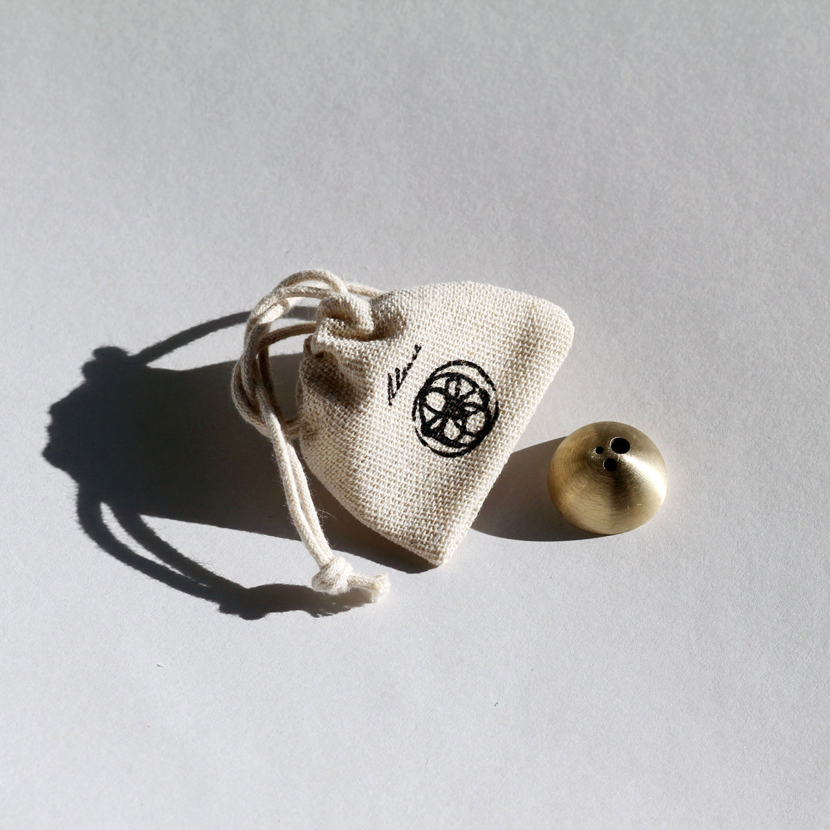 Small beige drawstring bag with a black symbol next to a brass object on a gray background