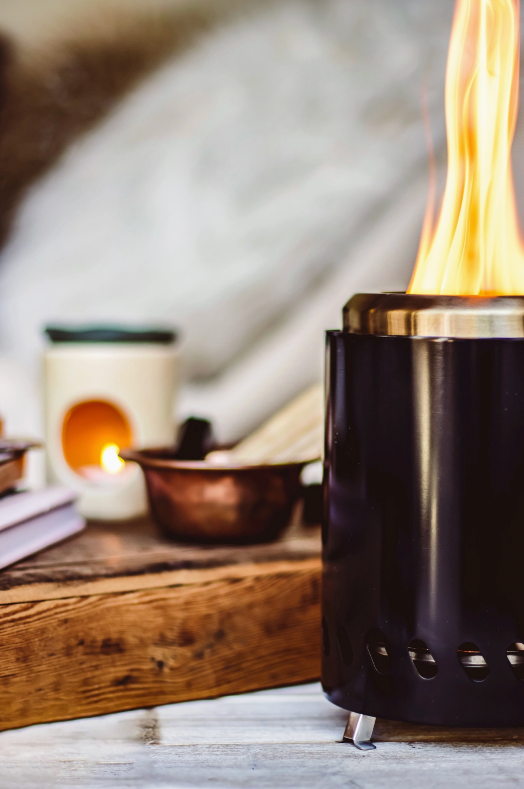 Black fire pit with flames on a wooden surface with candles and books in the background