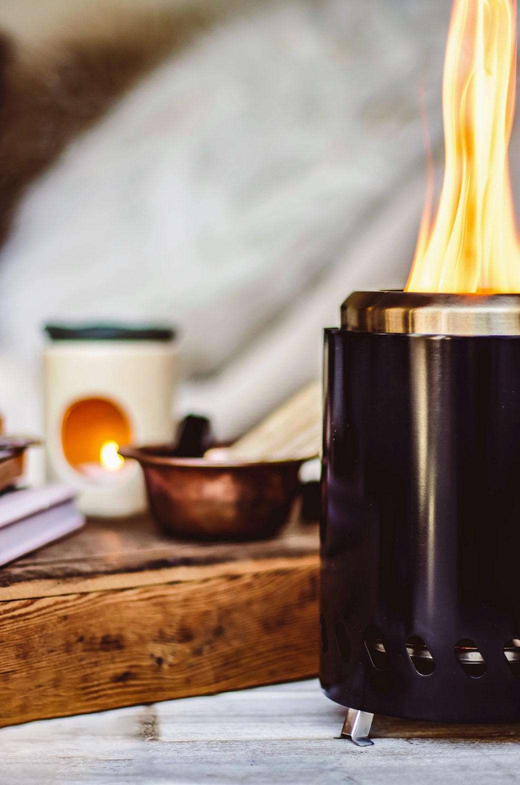 Black portable fireplace with flames on a wooden surface with candles and books in the background