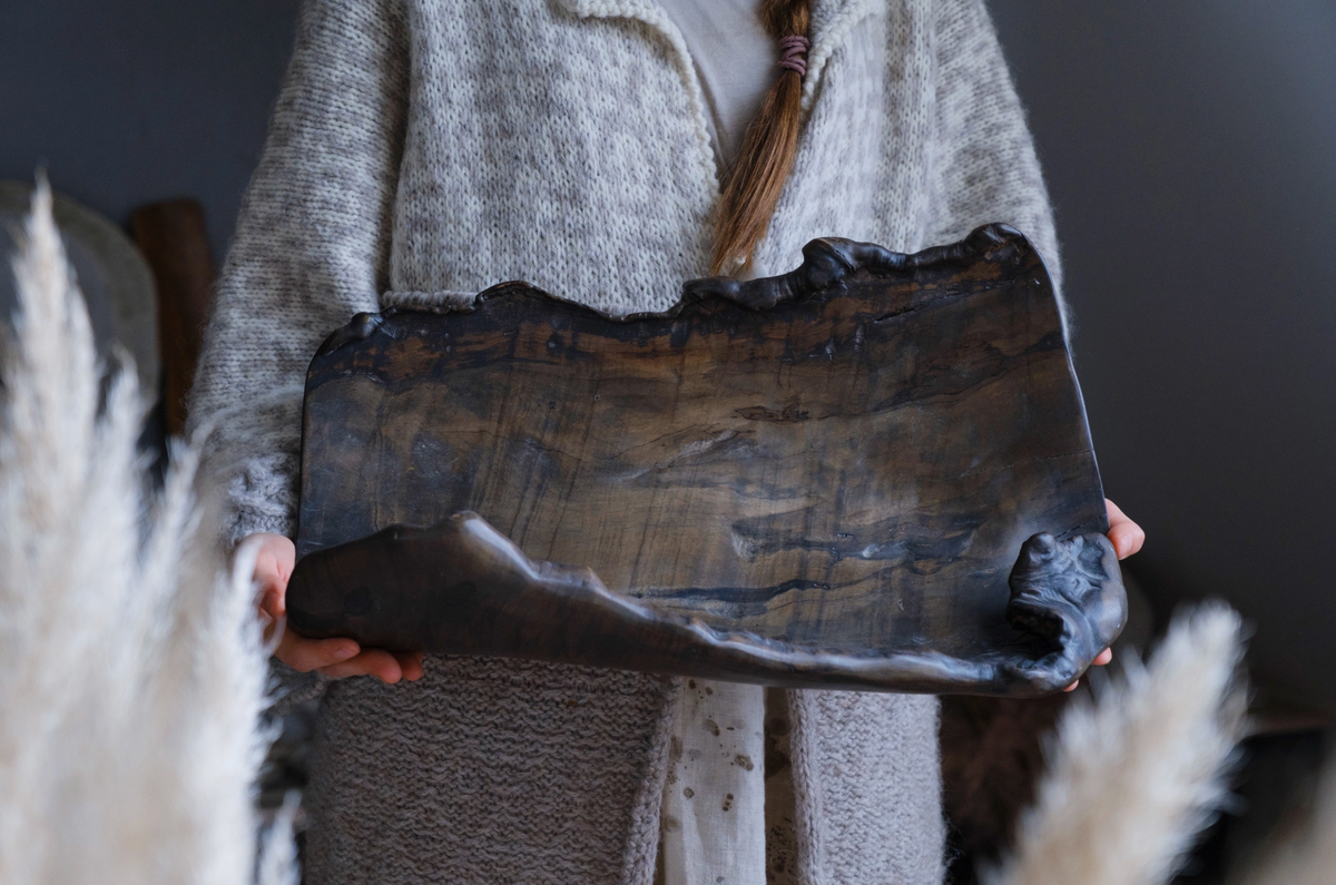 Person holding a large, rustic wooden tray with a neutral background