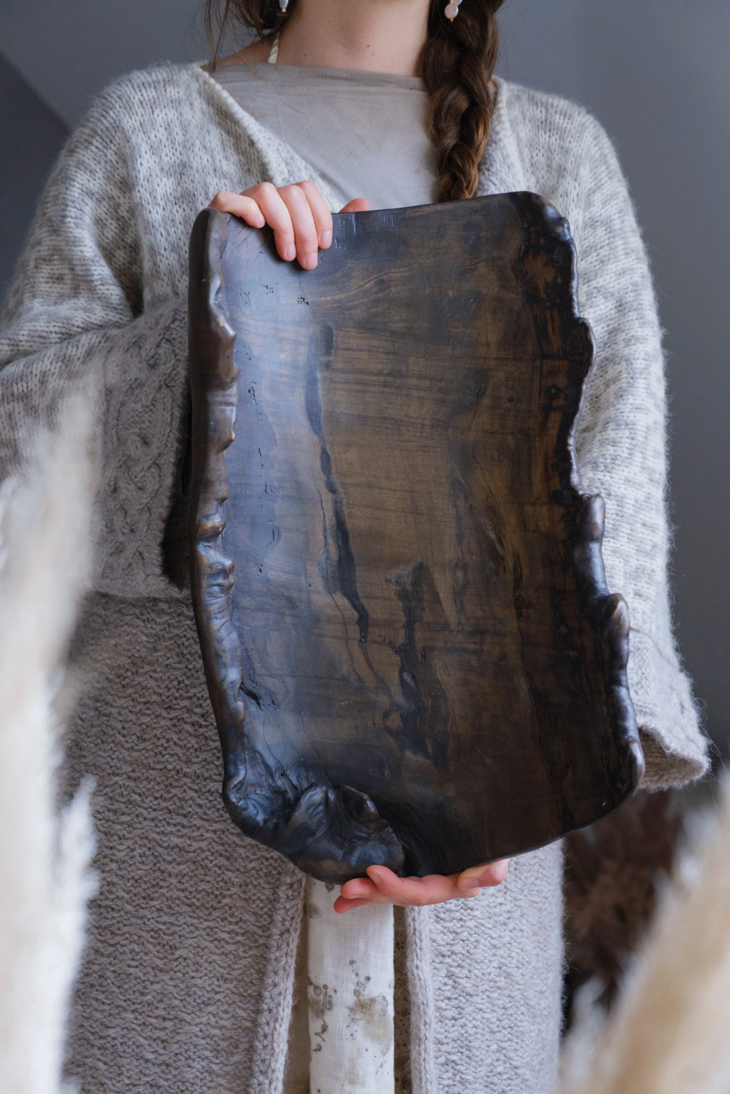 Person holding a dark wooden slab against a neutral background
