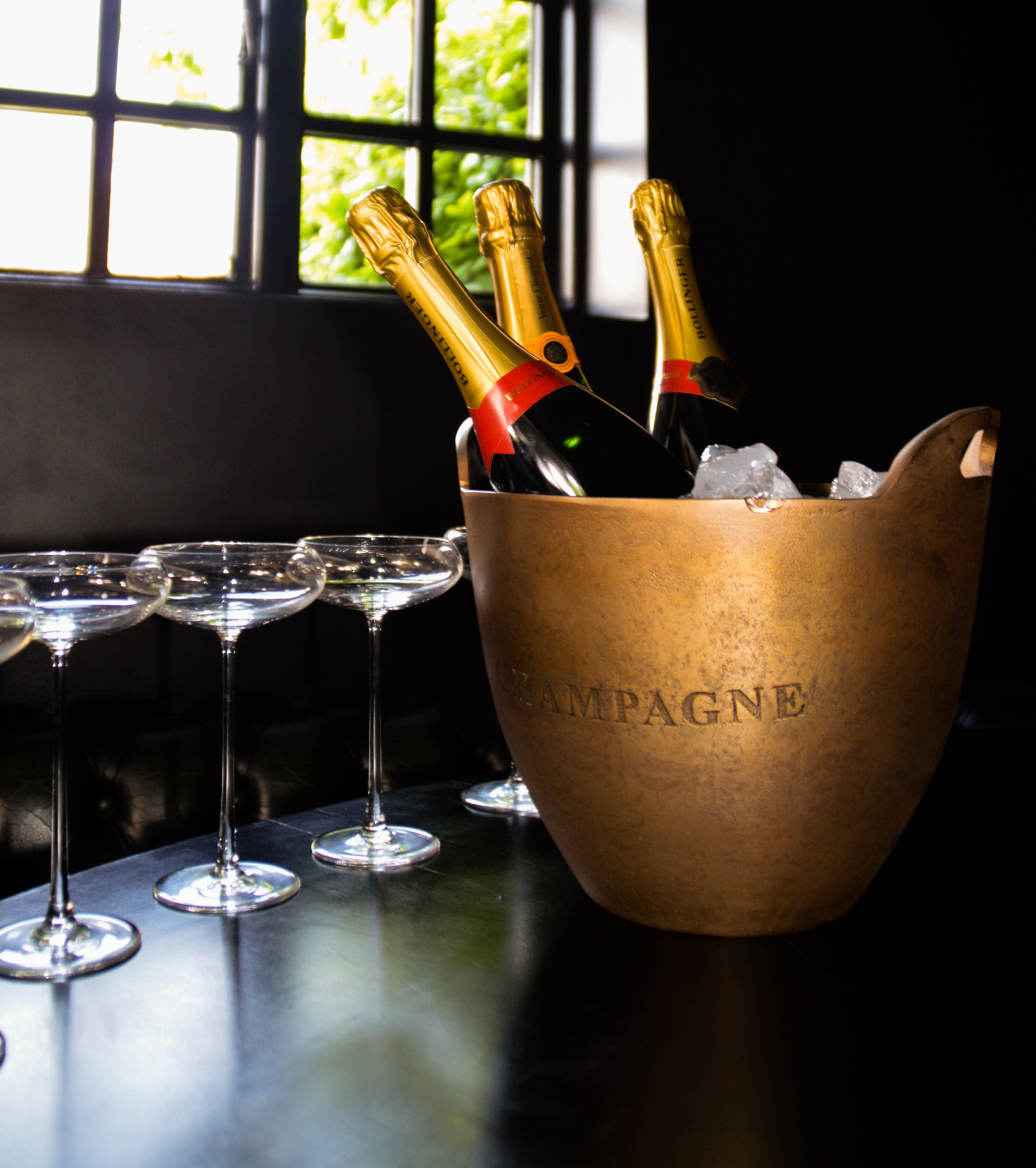 Two bottles of champagne in a bronze 'CAMPAGNE' ice bucket with champagne glasses on a table.