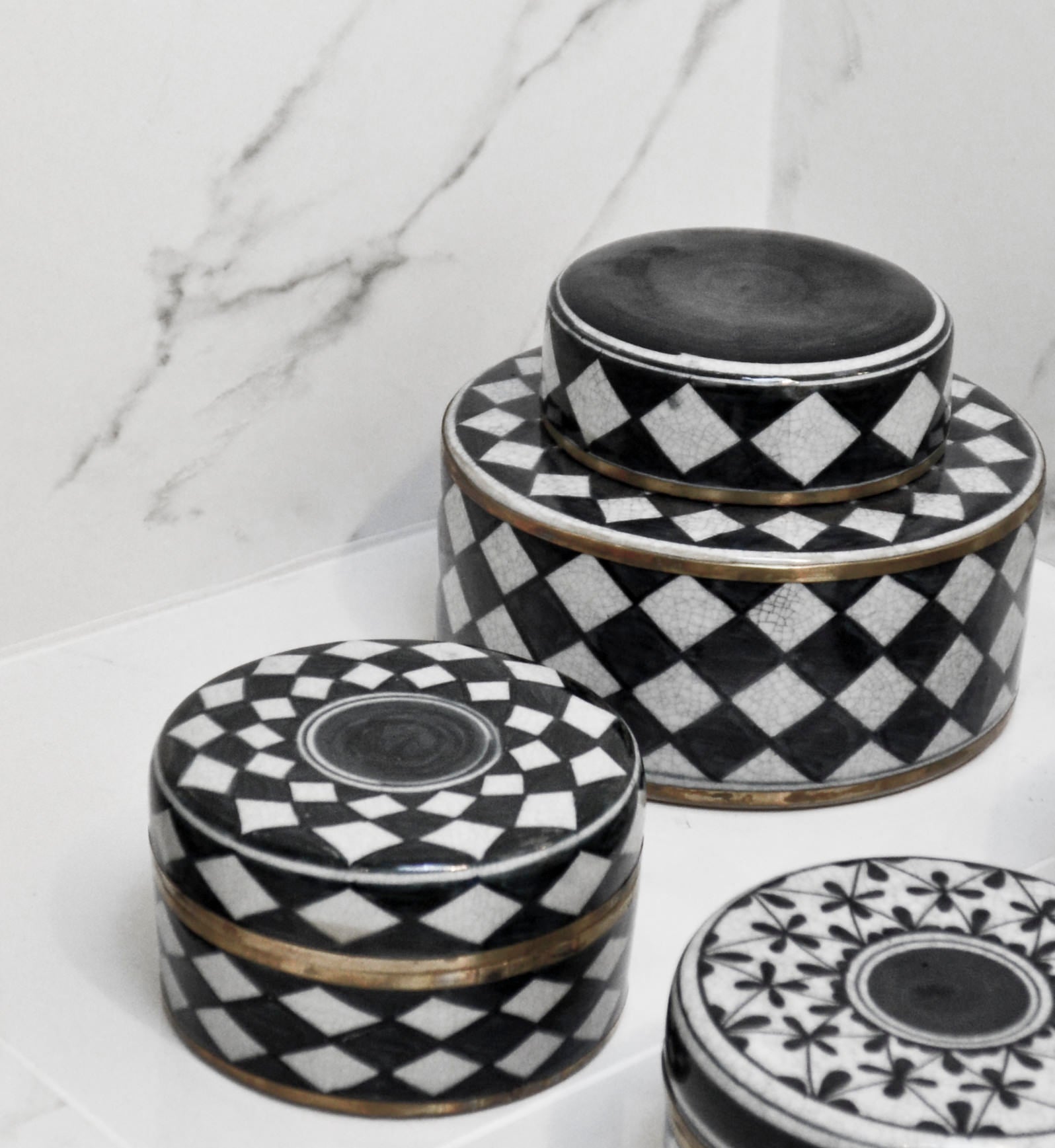 Set of three black and white patterned ceramic containers on a marble surface