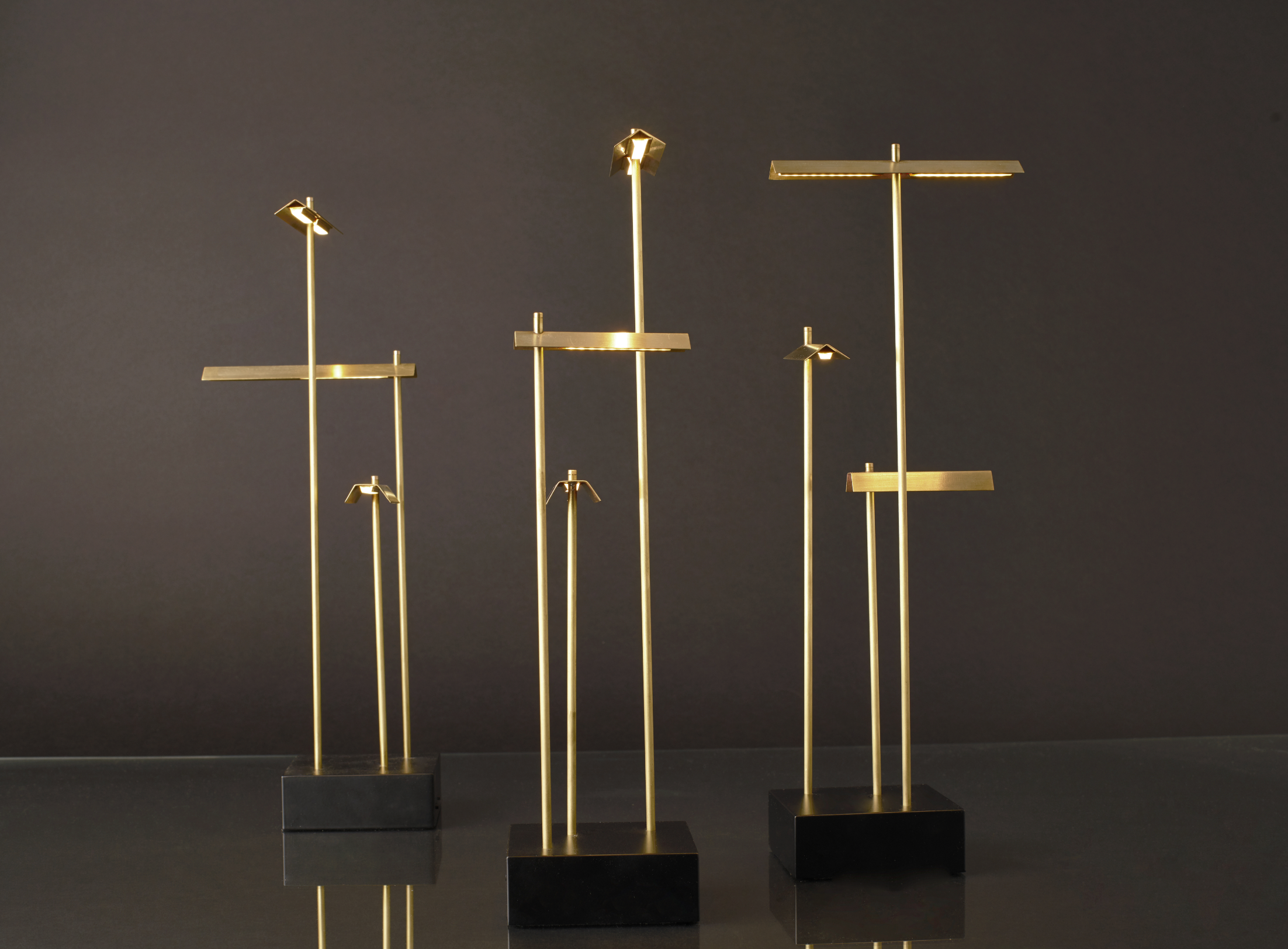 Set of four gold metal stands on black bases against a dark background