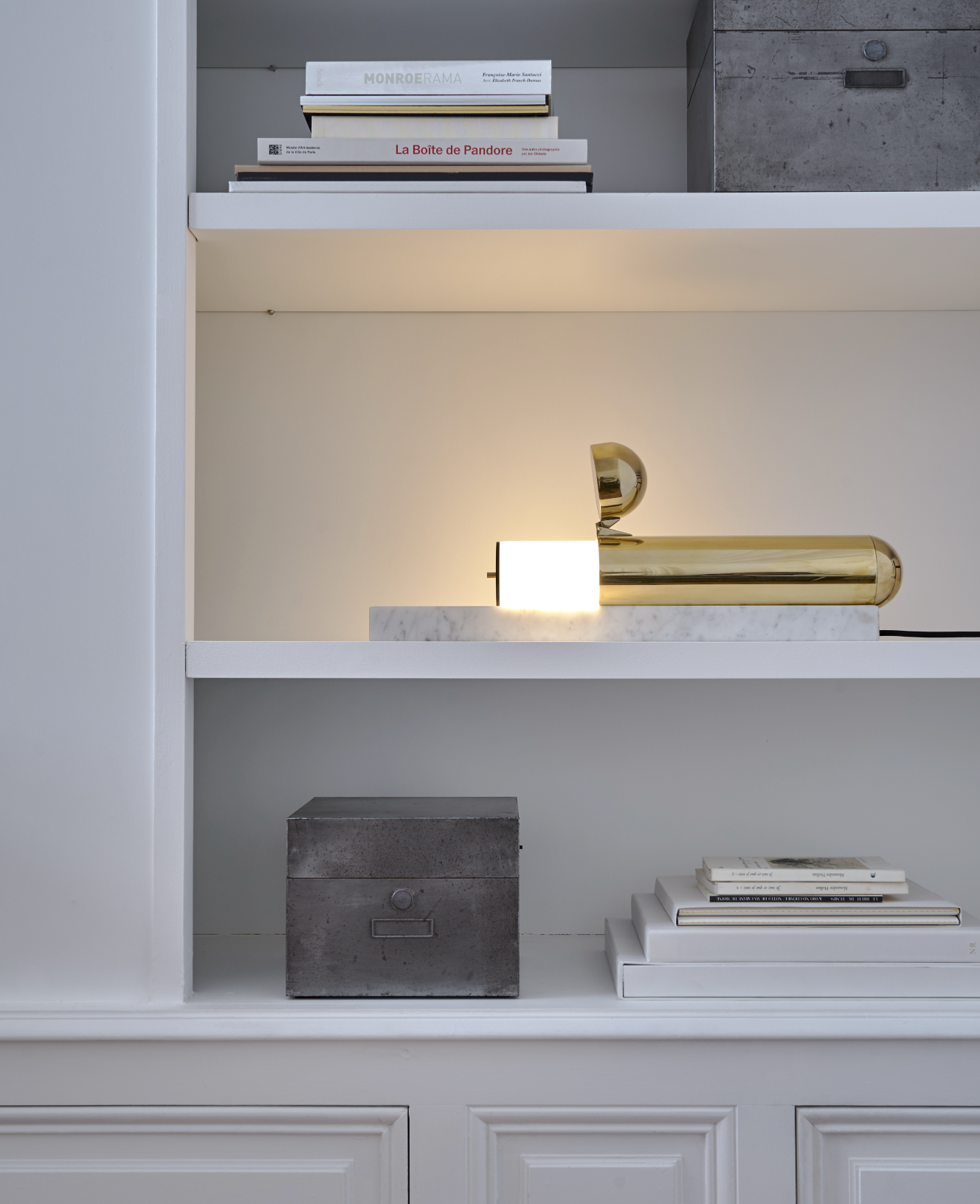 Gold wall-mounted lamp on a white shelf with books and decorative boxes.