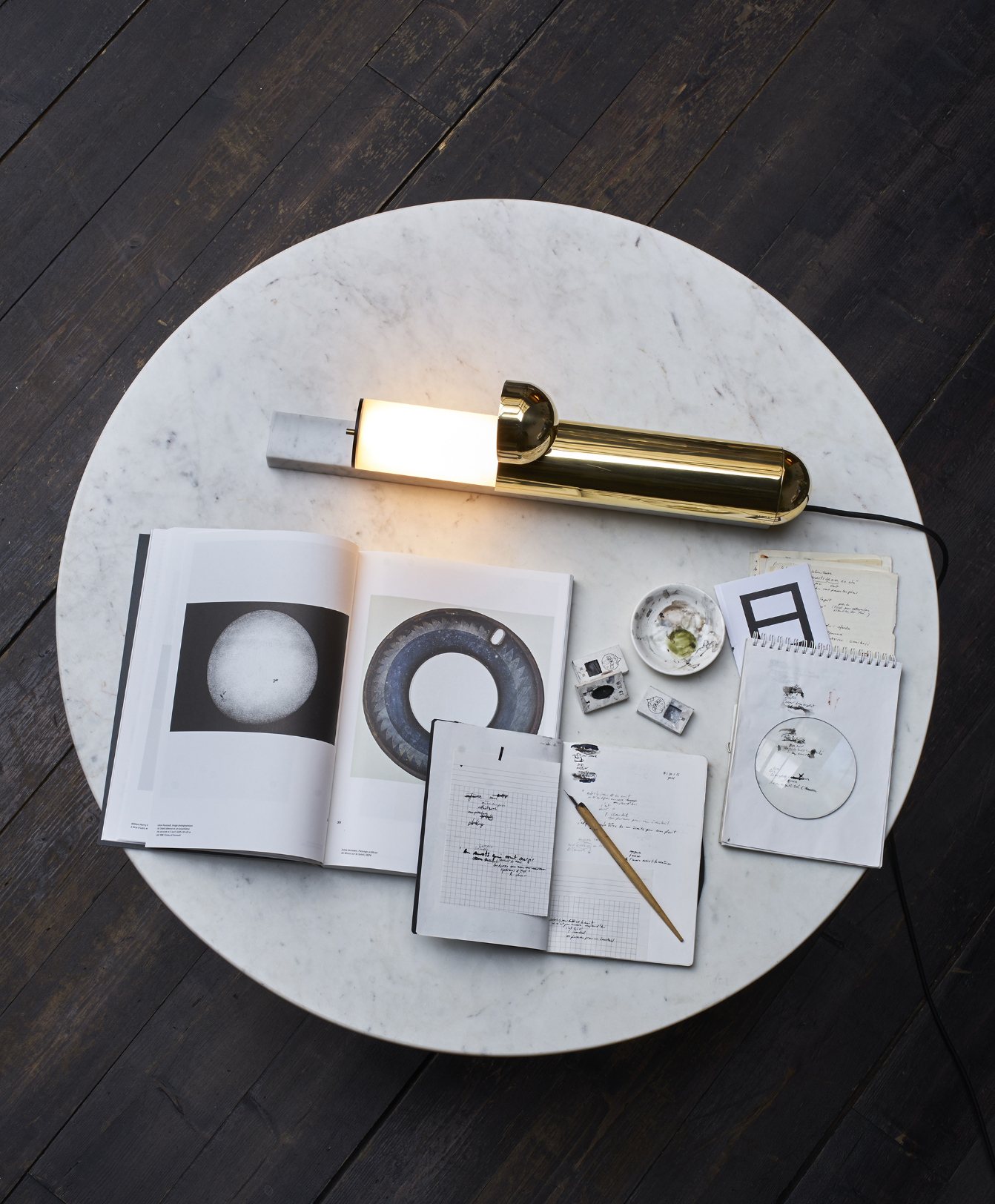 Round marble table with a gold lamp and various items on a dark wooden floor