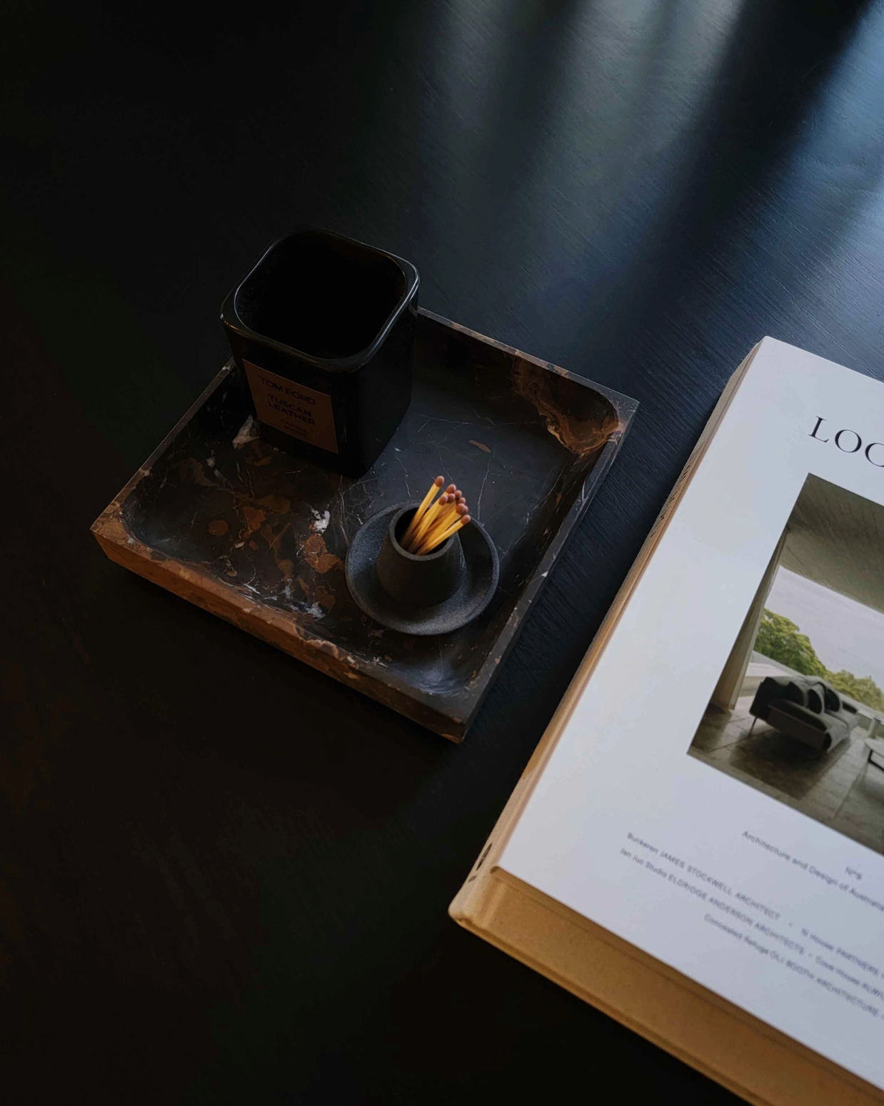 Tray with a candle and small object on a dark surface next to an open book.