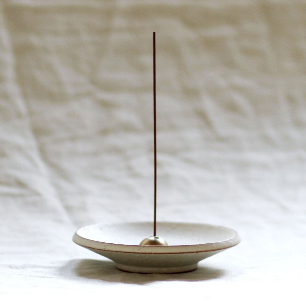 Ceramic incense holder with a single incense stick on a neutral background