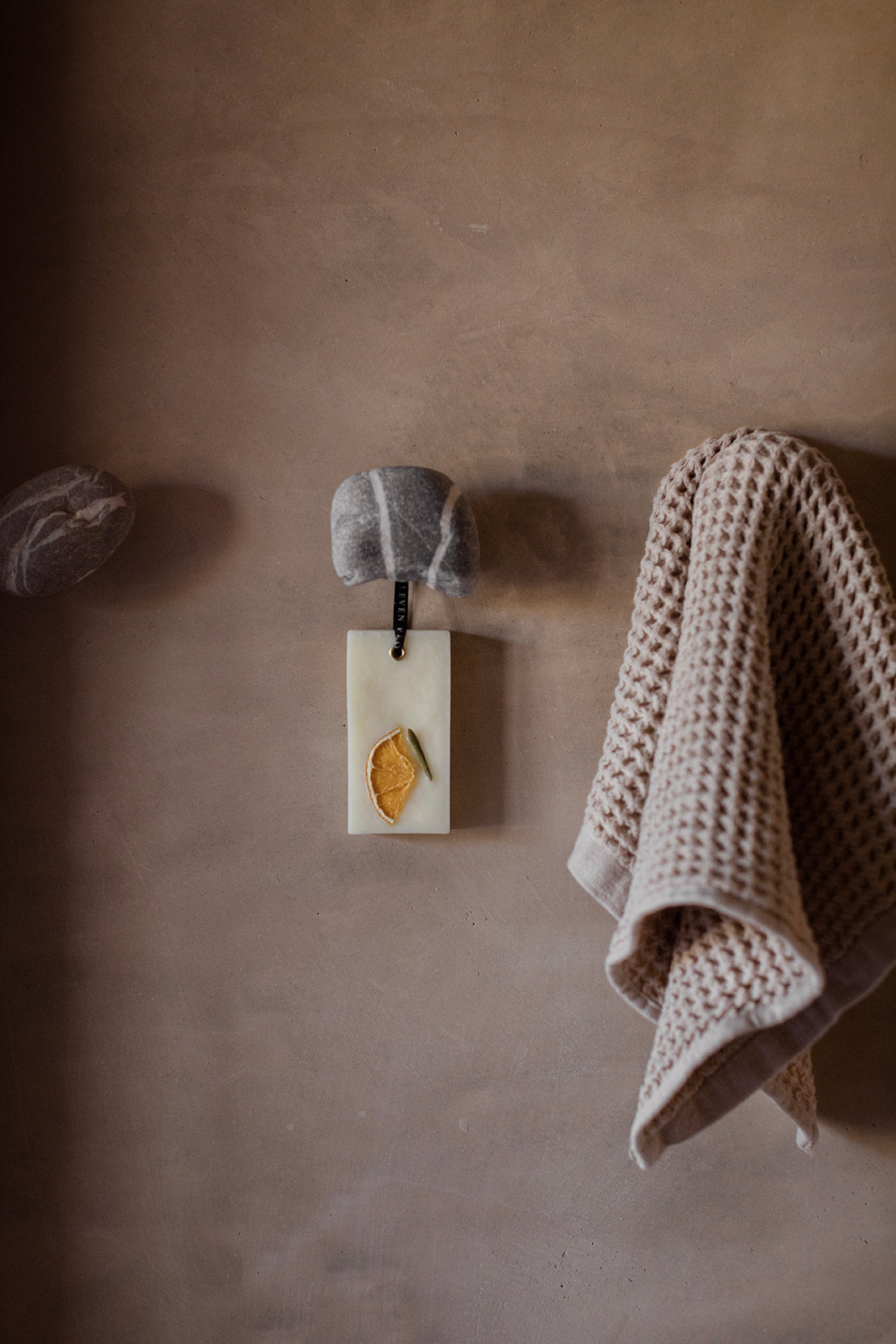 Decorative wall hook with a small rectangular plaque and a knitted towel on a brown wall.