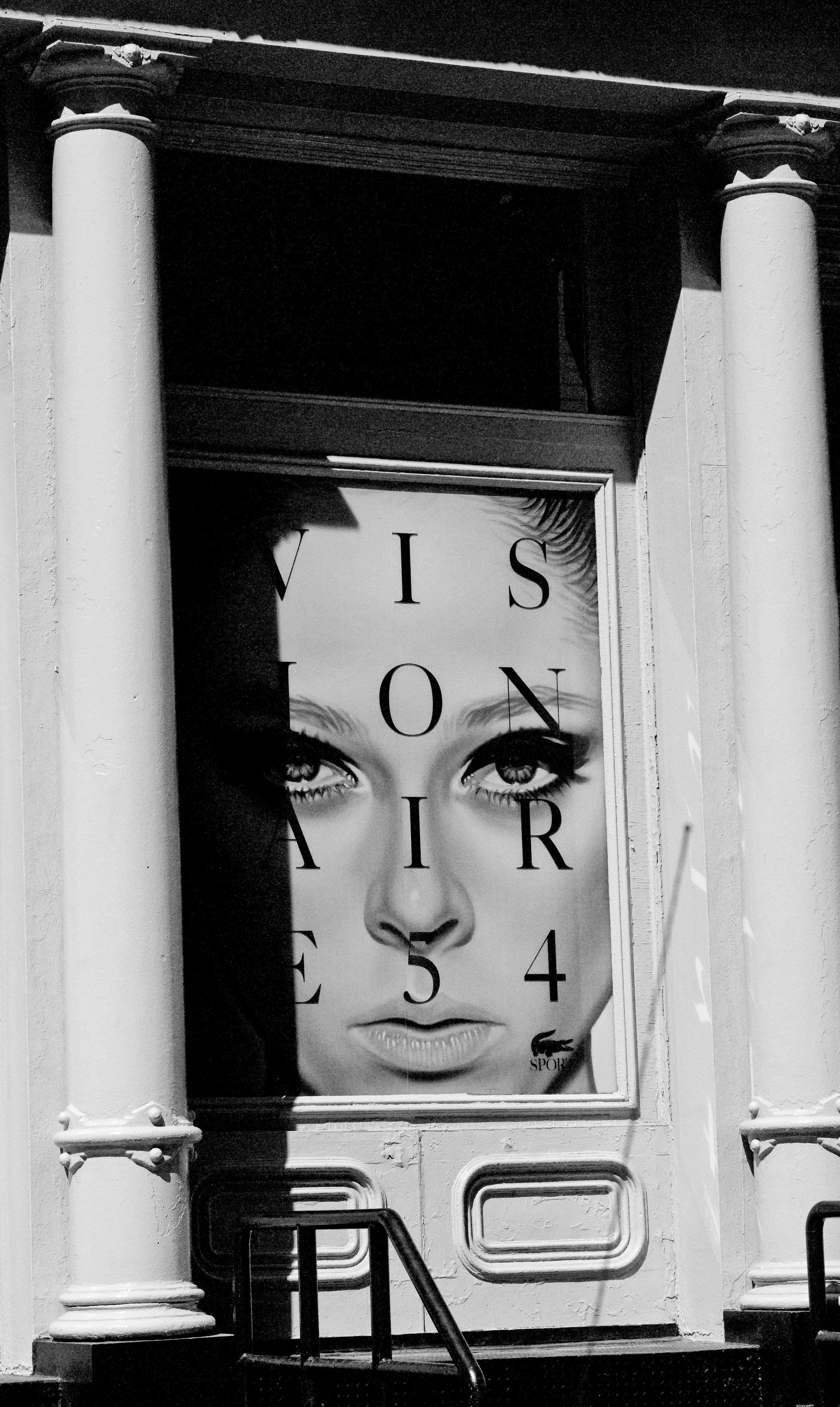 Black and white photo of a building facade with a large poster of a woman's face and text.