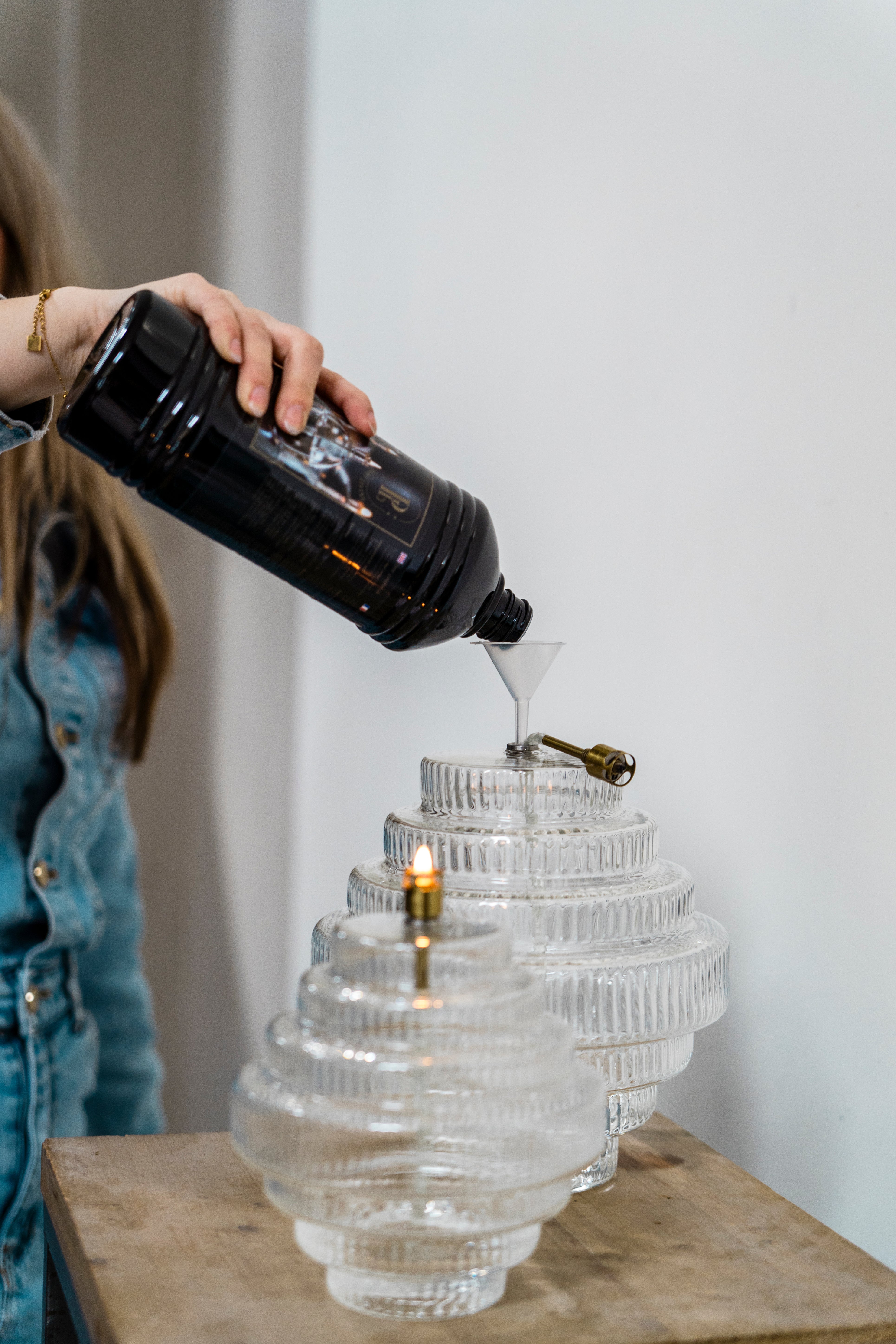 Person pouring liquid into a stack of glass lamps on a wooden surface.