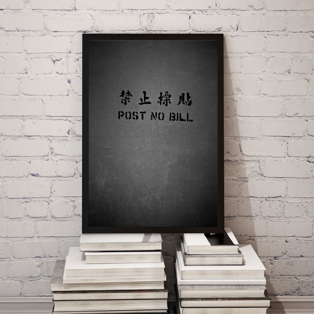 Black framed poster with text on a stack of books against a white brick wall.